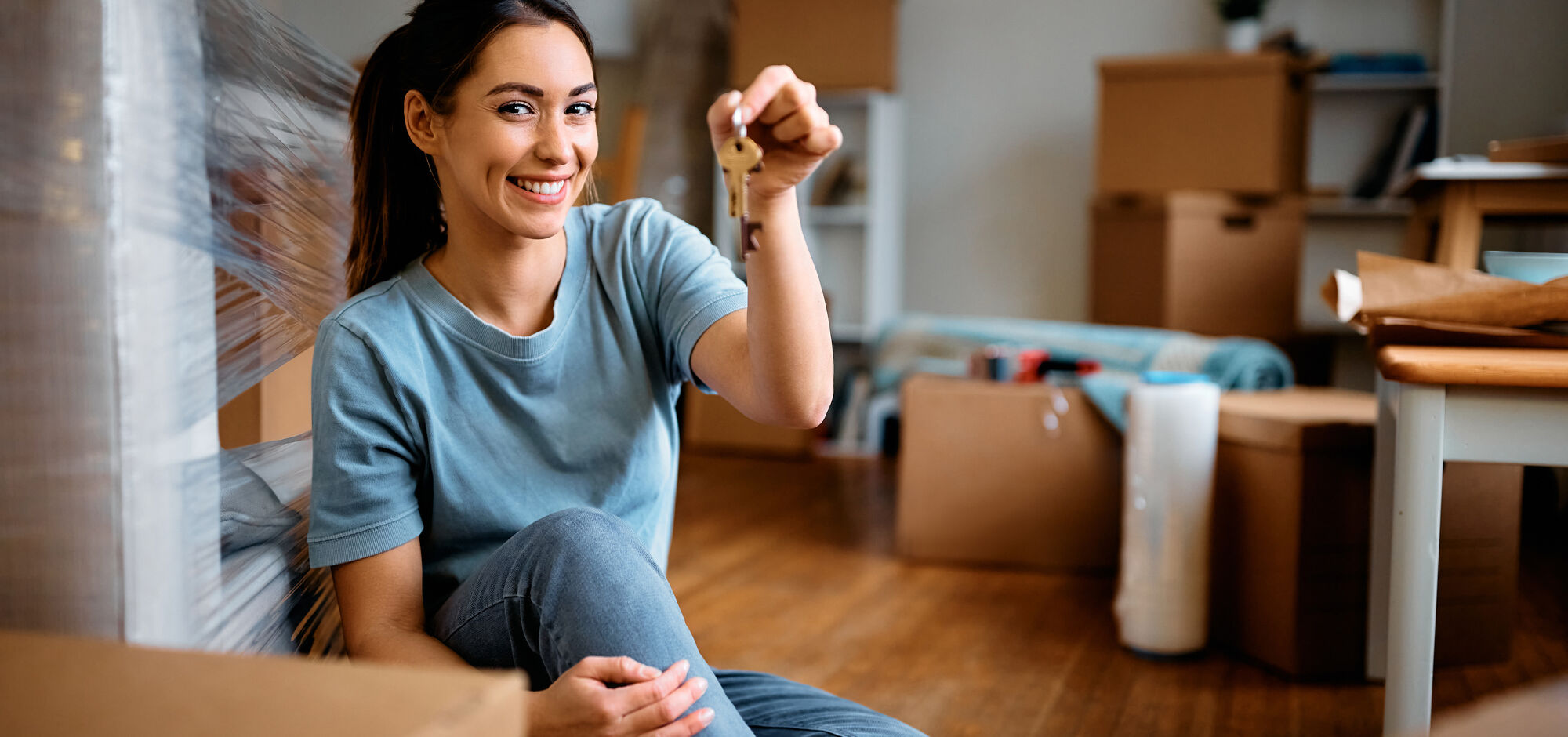 Young Happy Woman Holds Key While Moving Into New Home